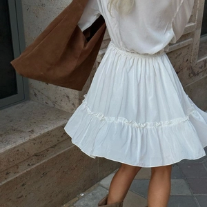 Detail of a white mini dress with ruffled hem and v-neck paired with a brown suede tote bag