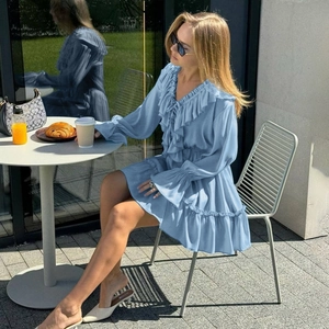 Close-up of a blue V-neck dress with ruffle details and flared sleeves in an outdoor setting
