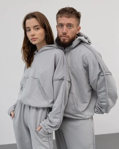 Détail d'un sweat à capuche gris avec coutures à bords francs et logo BACKSTAGE brodé