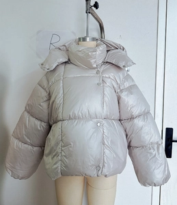 Détail d'une doudoune gris clair brillante avec large capuche et fermeture à pression