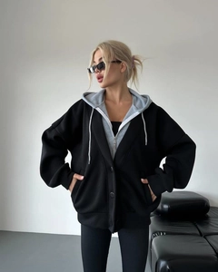 Detail eines schwarzen Oversize-Blazers mit grauer Kapuzenjacke in Lagenlook-Optik