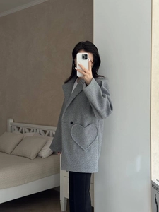 Detail of grey wool coat featuring a large heart-shaped patch pocket and button design