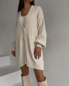 Detail of cable knit pattern and round button closure on off-white long cardigan