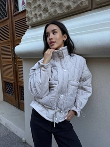 Detail of beige quilted jacket featuring stand collar and adjustable drawstring hemline