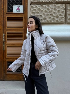 Close-up of quilted diamond pattern on beige stand collar jacket with drawstring hem detail