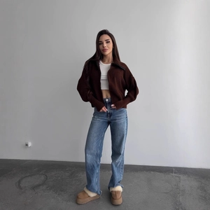 Dettaglio di un cardigan in maglia a costine marrone con zip e stivali in pelliccia platform