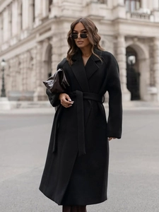 Classic black wool coat detail with waist belt and wide lapels against city backdrop