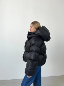 Détail d'une doudoune noire brillante à capuche avec surpiqûres et coupe surdimensionnée