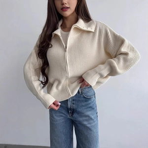 Dettaglio del cardigan in maglia crema con zip argentata e trama a coste in rilievo