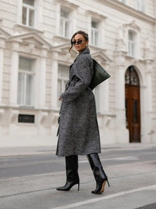 Outdoor street shot of a long grey herringbone wool coat with waist tie and black boots