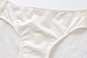 Close-up of silky beige fabric and delicate floral lace embroidery on women's low waist briefs