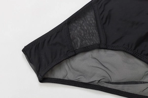 Detalle de sujetador negro en forma de U con paneles de malla y costuras en zigzag