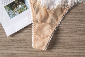 Détail d'un string en dentelle blanche et tulle couleur chair sur un support en bois