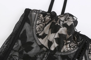 Detalle de bordado floral en corsé de encaje negro con aros y malla transparente
