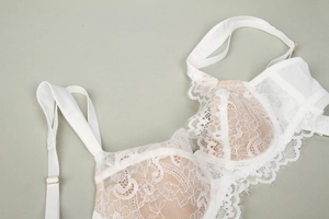 Detail of white eyelash lace bra with nude lining and adjustable gold buckles