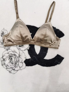 Detailed view of champagne satin triangle bra with pleated trim on soft white plush background