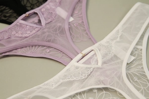 Close-up of floral embroidery on purple and white lace panties with metal ring details