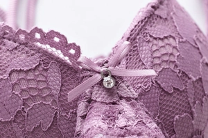 Detalle de sujetador de encaje morado con patrón floral, lazo y colgante de cristal
