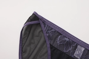Detalle de bordado morado sobre malla negra con encaje floral y costura elástica en zig-zag