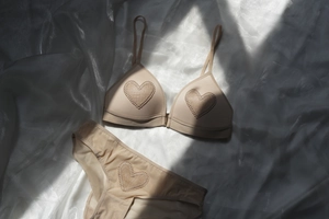 Primer plano detallado de lencería beige con bordado de corazón sobre fondo de seda suave