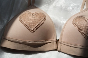 Detalle de sujetador beige sin aros con bordado de encaje de corazón y cierre frontal dorado