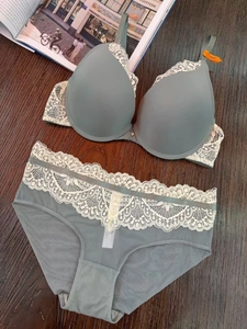 Ensemble lingerie en dentelle vert grisâtre avec broderies crème sur fond de bois