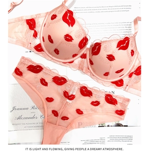 Dettaglio di reggiseno e slip in pizzo rosa con ricamo a labbra rosse su rete