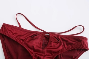 Close-up of wine red satin panties featuring lace patchwork and a delicate bow detail