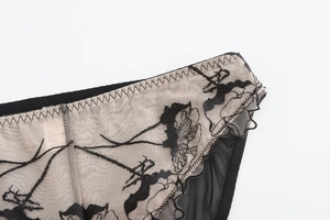 Détail d'une broderie florale noire sur résille transparente avec bordure en dentelle festonnée