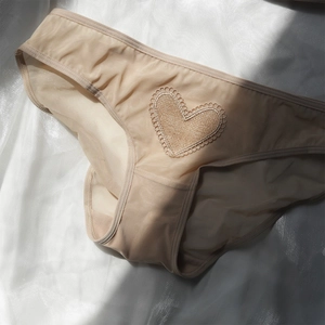 Dettaglio di slip in rete beige con ricamo in pizzo a cuore su sfondo di seta lucida