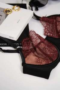 Flat lay of wine red lace bra with black satin trim and gold metal hardware detail