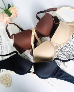 Tre reggiseni push-up senza cuciture neri, beige e marroni su sfondo di giornale
