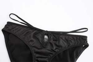 Détail d'une culotte en satin noir avec design à lanières et bordure en dentelle