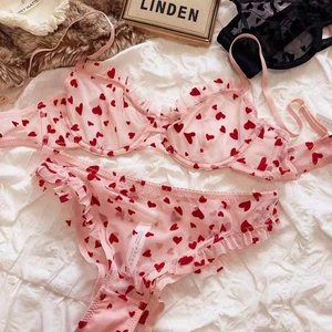 Dettaglio del set di lingerie in mesh rosa con stampa a cuori rossi e bordi a balze