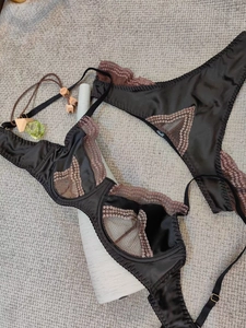Detail of black satin bra set with brown lace trim and matching panties in a flat lay view