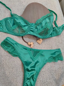 Flat lay of emerald green satin bra and thong set with delicate eyelash lace detailing
