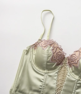 Dettaglio corsetto in raso verde chiaro con ricamo rosa e design a rete stringato