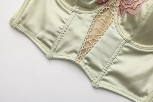 Primo piano di un corsetto verde salvia con ricamo floreale rosa e dettagli in pizzo