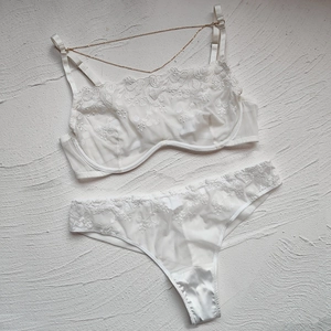 Detail of white lace lingerie set featuring delicate floral embroidery and gold chain strap