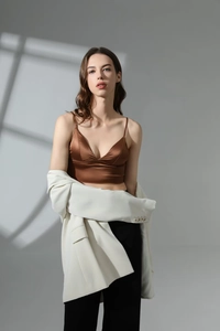 Dettaglio del bralette in raso marrone scuro abbinato a blazer bianco e pantaloni neri
