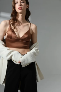 Dettaglio ravvicinato di un top in raso bronzo con scollo a V e blazer bianco oversize