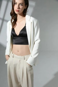 Detail of black satin camisole top paired with white blazer and beige linen trousers