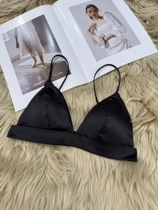 Detail of black silk satin triangle bralette with thin straps on soft texture background