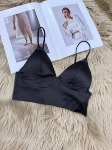 Detail of black satin triangle bralette with thin straps on a soft plush background