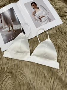 Detail of pearl white satin bralette with thin straps on brown plush rug background