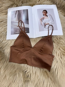 Detail view of brown satin wireless bra with thin straps on soft textured background