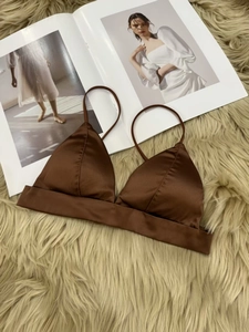 Detail of chocolate brown satin bralette featuring a thin strap on a plush white rug