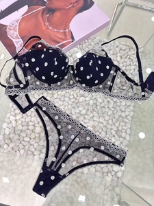 Flat lay of black polka dot lace bra and panty set on a white pebble background