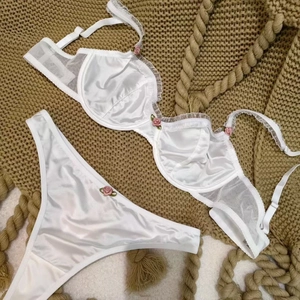 White satin and lace lingerie set with pink 3D roses on soft green knit background