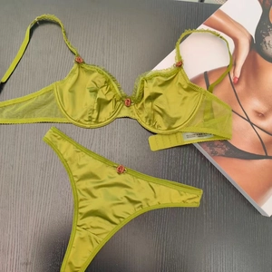 Olive green silk lace lingerie set with red rose details on a dark wood background